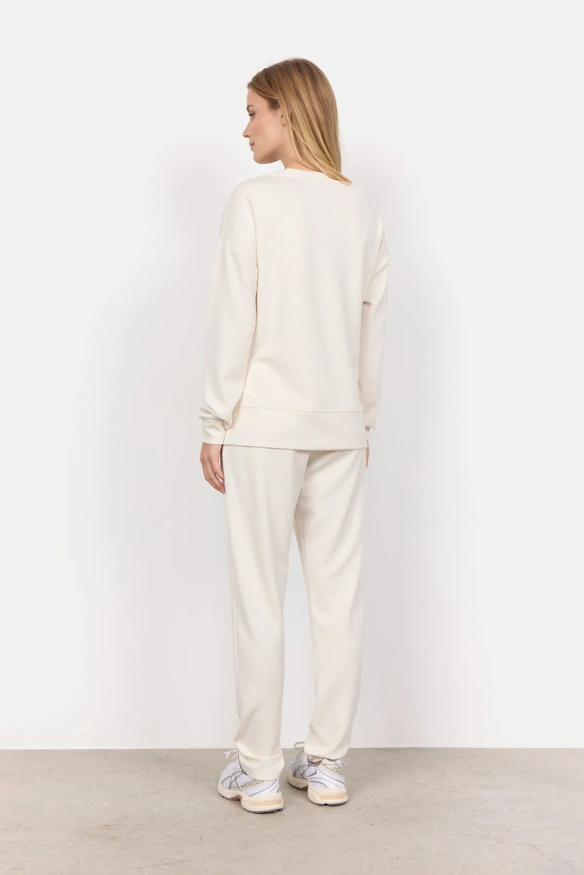Wearing the Soya Concepts Banu Long Sleeve Sweater in off-white, paired with matching pants, this individual showcases relaxed style and all-day comfort against a simple backdrop.
