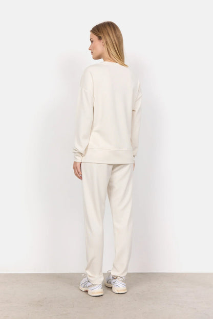 Wearing the Soya Concepts Banu Long Sleeve Sweater in off-white, paired with matching pants, this individual showcases relaxed style and all-day comfort against a simple backdrop.