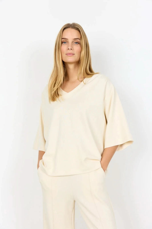 A woman with long blonde hair wears the Soya Concepts Banu Top, its elegant silhouette highlighted as she stands against a plain white background.