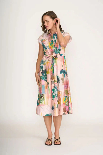 A woman wears the Foil Atrium Dress—a light pink, short-sleeve midi dress with a vibrant tropical print—against a plain white background.
