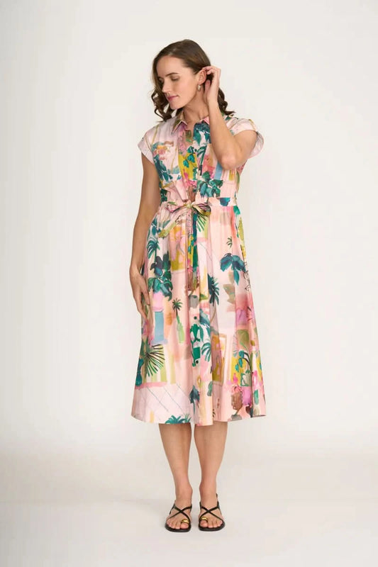 A woman wears the Foil Atrium Dress—a light pink, short-sleeve midi dress with a vibrant tropical print—against a plain white background.
