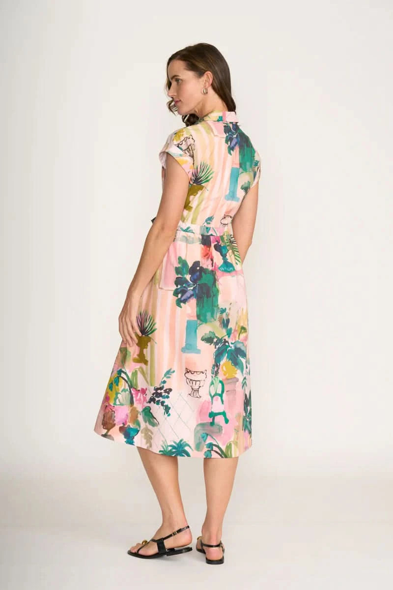 A woman wears the Foil Atrium Dress—a light pink, short-sleeve midi dress with a vibrant tropical print—against a plain white background.