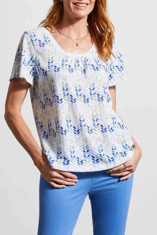 Woman wearing a stylish Tribal printed flutter sleeve blouse in white and blue pattern with blue pants, smiling.