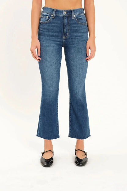 A person wearing Daze's Shy Girl High Rise Crop Flare jeans in denim blue and black ballet flats is standing against a plain white background.