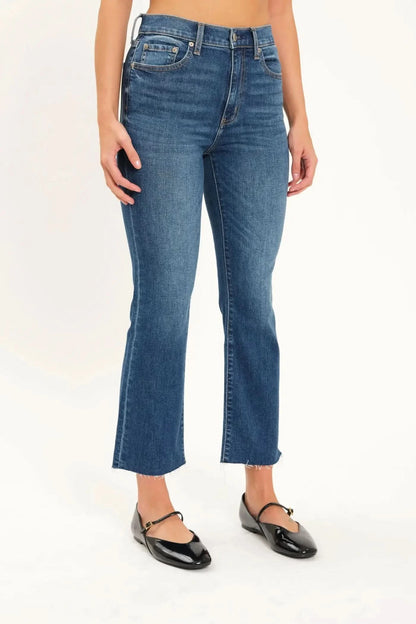 A person wearing Daze's Shy Girl High Rise Crop Flare jeans in denim blue and black ballet flats is standing against a plain white background.