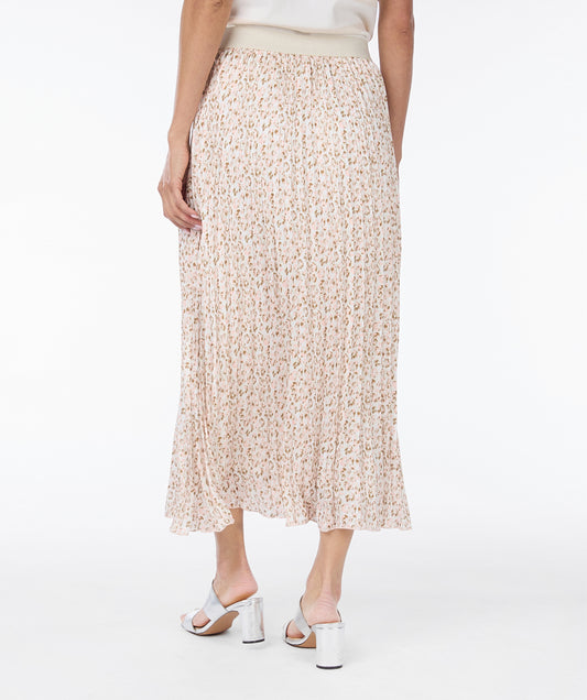 A woman stands against a white background, wearing a light-colored striped top, an Esqualo Pastel Skirt with a flattering fit, and silver sandals. She is smiling and holding the hem of her Esqualo skirt with one hand, showcasing her stylish look.