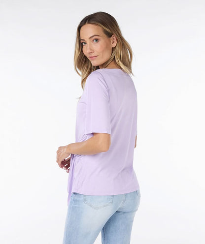 Woman wearing a cute and comfortable Lilac Top by Esqualo with a tie-front detail, paired with light blue jeans made from high-quality materials, posing against a plain white background.