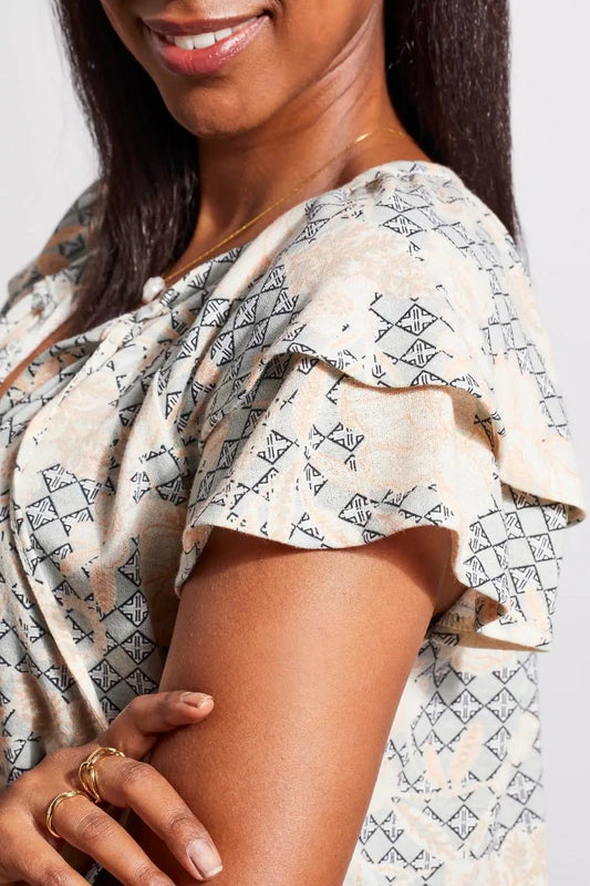 A woman wearing a stylish Tribal Short Sleeve Peasant Top with ruffled sleeves and white cotton pants.