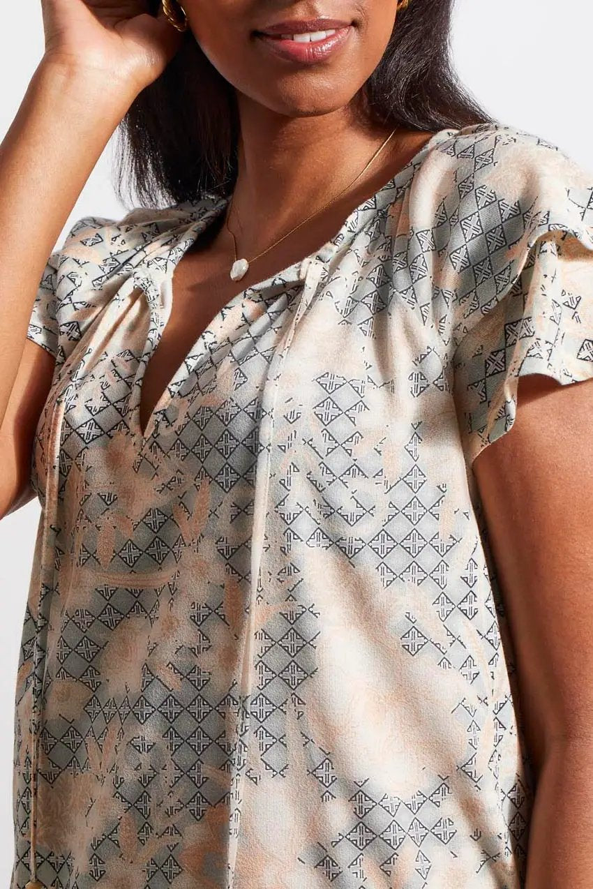 A woman wearing a stylish Tribal Short Sleeve Peasant Top with ruffled sleeves and white cotton pants.