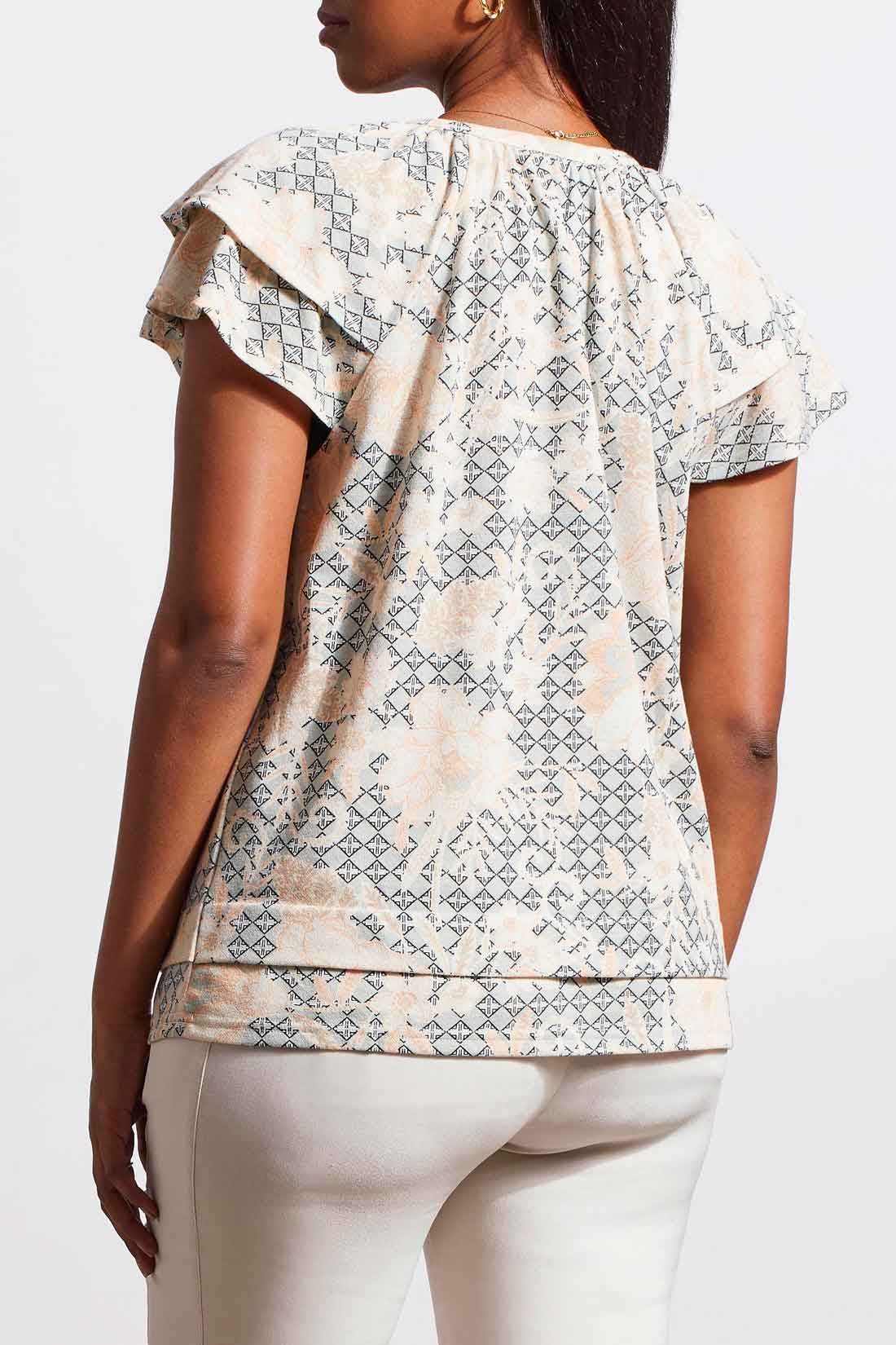 A woman wearing a stylish Tribal Short Sleeve Peasant Top with ruffled sleeves and white cotton pants.