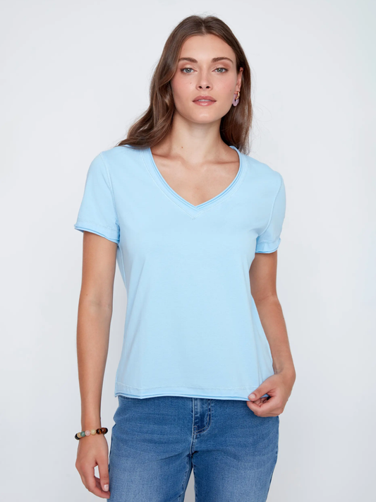A woman models the CoCo Y Club T-shirt V-neck in light blue with blue jeans against a plain white background, highlighting this essential piece.