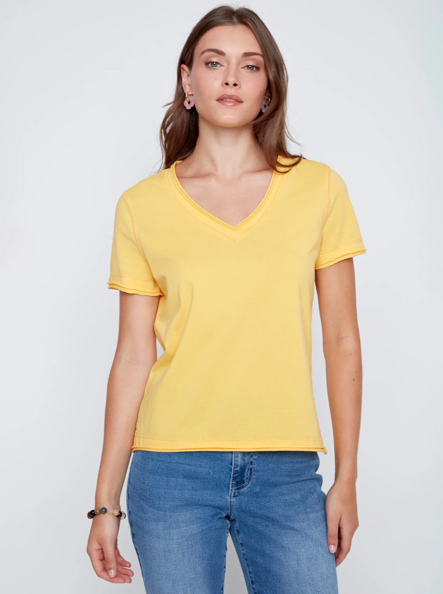 A woman models the CoCo Y Club T-shirt V-neck in light blue with blue jeans against a plain white background, highlighting this essential piece.