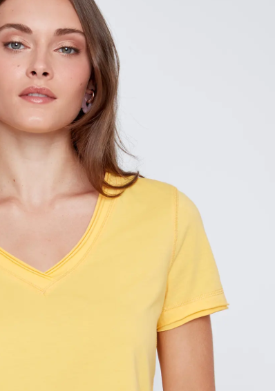 A woman models the CoCo Y Club T-shirt V-neck in light blue with blue jeans against a plain white background, highlighting this essential piece.