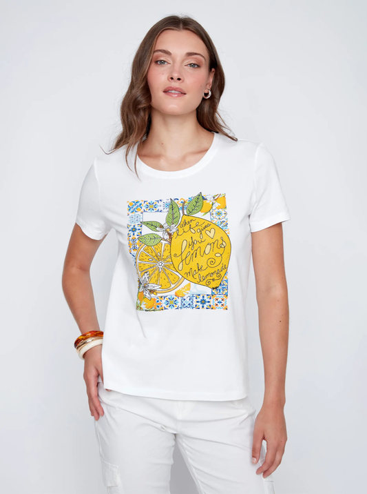 A woman wears a CoCo Y Club short-sleeved T-shirt featuring a colorful lemon print and text, paired with white pants—creating a fresh summer look. The outfit is shown against a plain white background.
