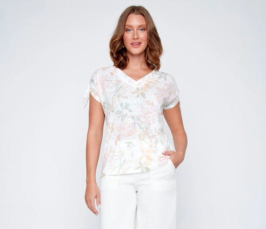 A woman models the CoCo Y Club V-neck top, a light floral, short-sleeve blouse, paired with white pants. The perfect spring-summer choice for effortless style.