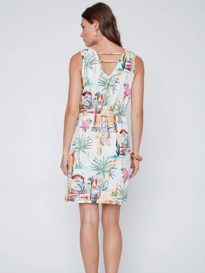 A woman models the CoCo Y Club Mini Palm Dress, a sleeveless, knee-length dress with a vibrant tropical print, set against a plain light gray background.