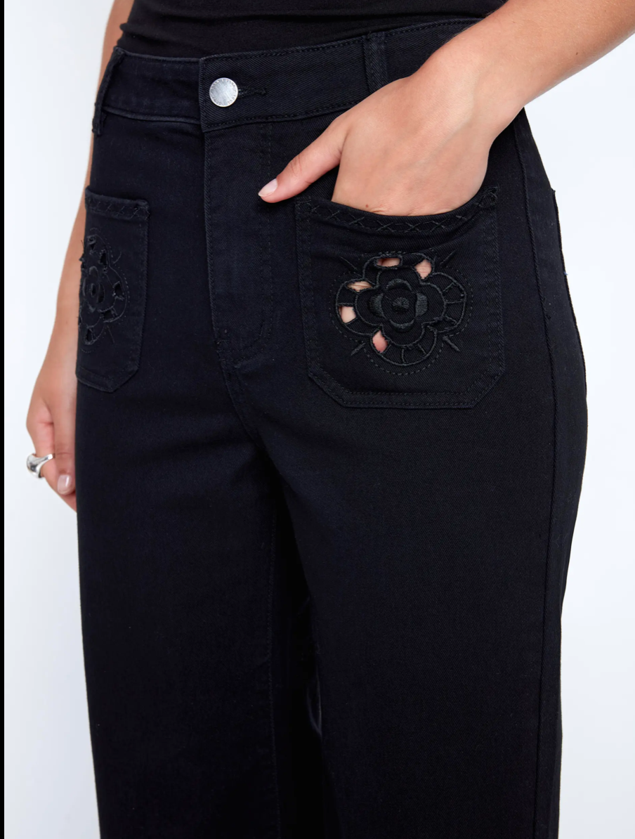 A woman in a black sleeveless top and CoCo Y Club Embroidered Black Trousers holds a silver clutch and wears silver slip-on shoes, standing against a plain white background.