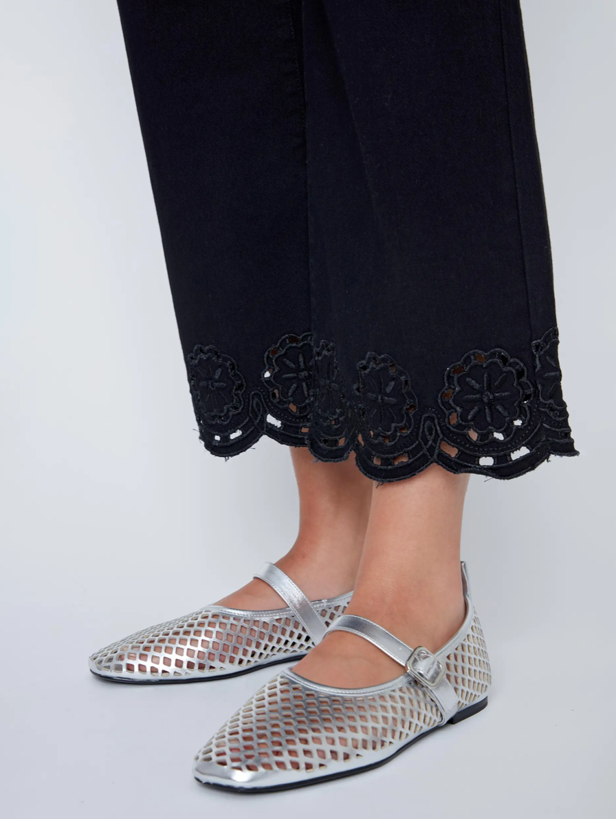 A woman in a black sleeveless top and CoCo Y Club Embroidered Black Trousers holds a silver clutch and wears silver slip-on shoes, standing against a plain white background.