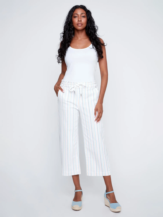 A woman stands against a plain background in a white tank top and CoCo Y Club's Zipless Trousers—high-waisted, striped, with an elasticated waistband—paired with light blue espadrille wedges for a fresh summer look.