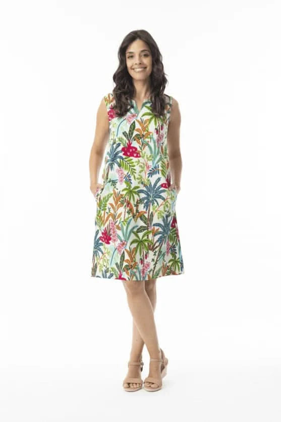 A woman stands against a white background wearing the Orientique Ovahe Sleeveless Shift Dress, featuring a colorful tropical floral pattern and boat neckline, paired with beige sandals.