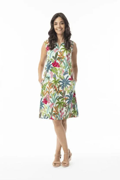 A woman stands against a white background wearing the Orientique Ovahe Sleeveless Shift Dress, featuring a colorful tropical floral pattern and boat neckline, paired with beige sandals.