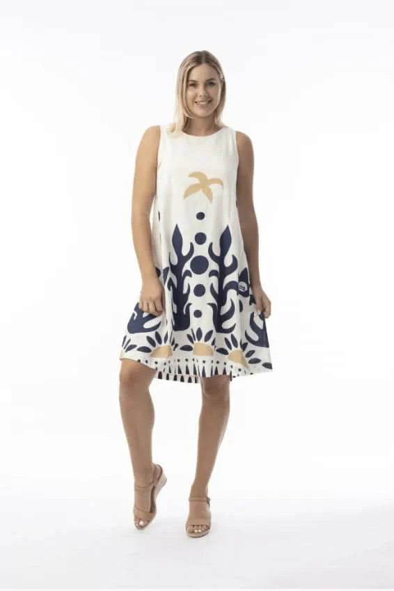 A woman in an Orientique Nazca Sleeveless Midi Dress with bold blue and tan abstract patterns and a flared hem stands by a black iron fence on a sunny day.