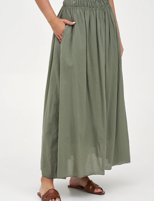 A woman wears the M Made In Italy Woven Maxi Skirt in olive green, featuring an elastic waistband and side pockets, made from breathable fabric, styled with brown flat sandals.