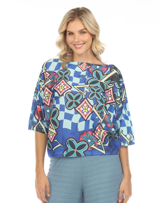 A person with shoulder-length blonde hair is shown from behind, wearing the Inoah 3/4 Sleeve Dolman Sweater featuring a colorful geometric and floral pattern, paired with blue textured pants.