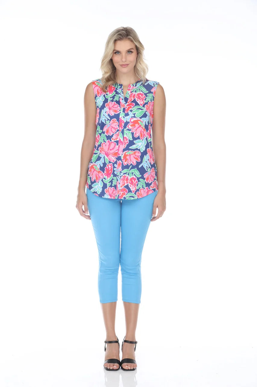 A person stands confidently against a white backdrop, smiling with one hand on their hip, wearing the feminine Rose Sleeveless Floral Top by Tango Mango made from wrinkle-resistant fabric, paired with stylish blue pants.
