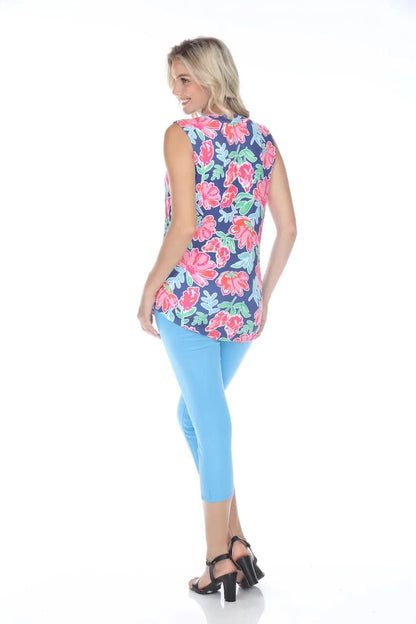 A person stands confidently against a white backdrop, smiling with one hand on their hip, wearing the feminine Rose Sleeveless Floral Top by Tango Mango made from wrinkle-resistant fabric, paired with stylish blue pants.