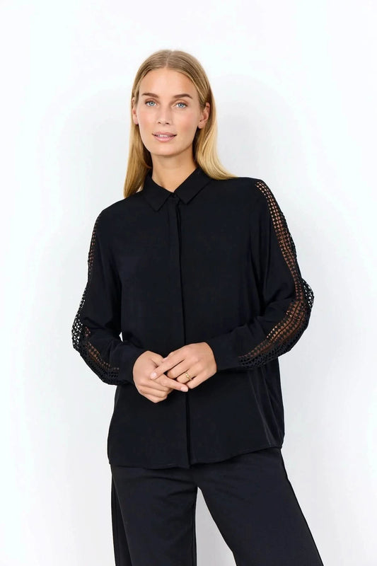 A woman stands against a plain background wearing the Soya Concepts Ladies Woven Blouse—a black, lightweight viscose blouse with lace long sleeves—paired with black pants.