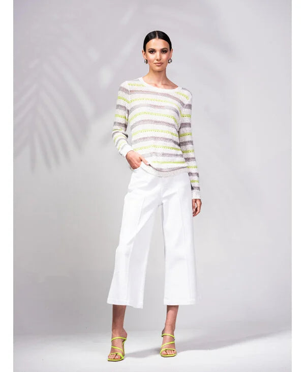 A person is wrapped in an Alison Sheri Striped Knit Sweater with green and white stripes, perfectly paired with white pants. The plain light gray background enhances the outfit's versatile and trendy appeal.