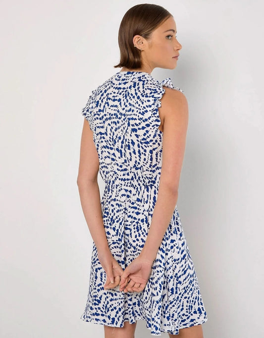 A woman stands against a white background wearing the Apricot Wavy Spot Button Up Dress, ideal for summer with blue abstract dot patterns and ruffled short sleeves.