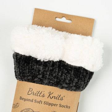 A woman sitting on a chair wearing Cray Cray Soft Slipper Socks, the slip-proof chenille fuzzy socks from Britt's Knits.