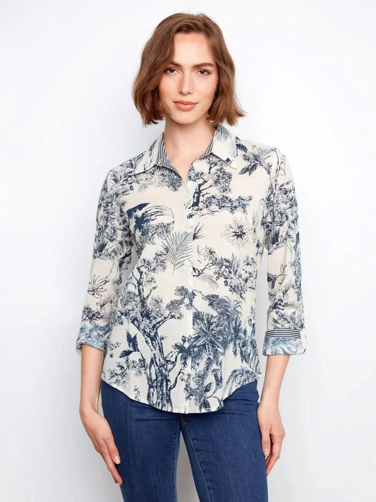 A woman wears a Charlie B Printed Cotton Voile Button-Up Blouse with a blue and white botanical pattern, paired with blue jeans, standing against a plain light background.