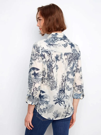 A woman wears a Charlie B Printed Cotton Voile Button-Up Blouse with a blue and white botanical pattern, paired with blue jeans, standing against a plain light background.