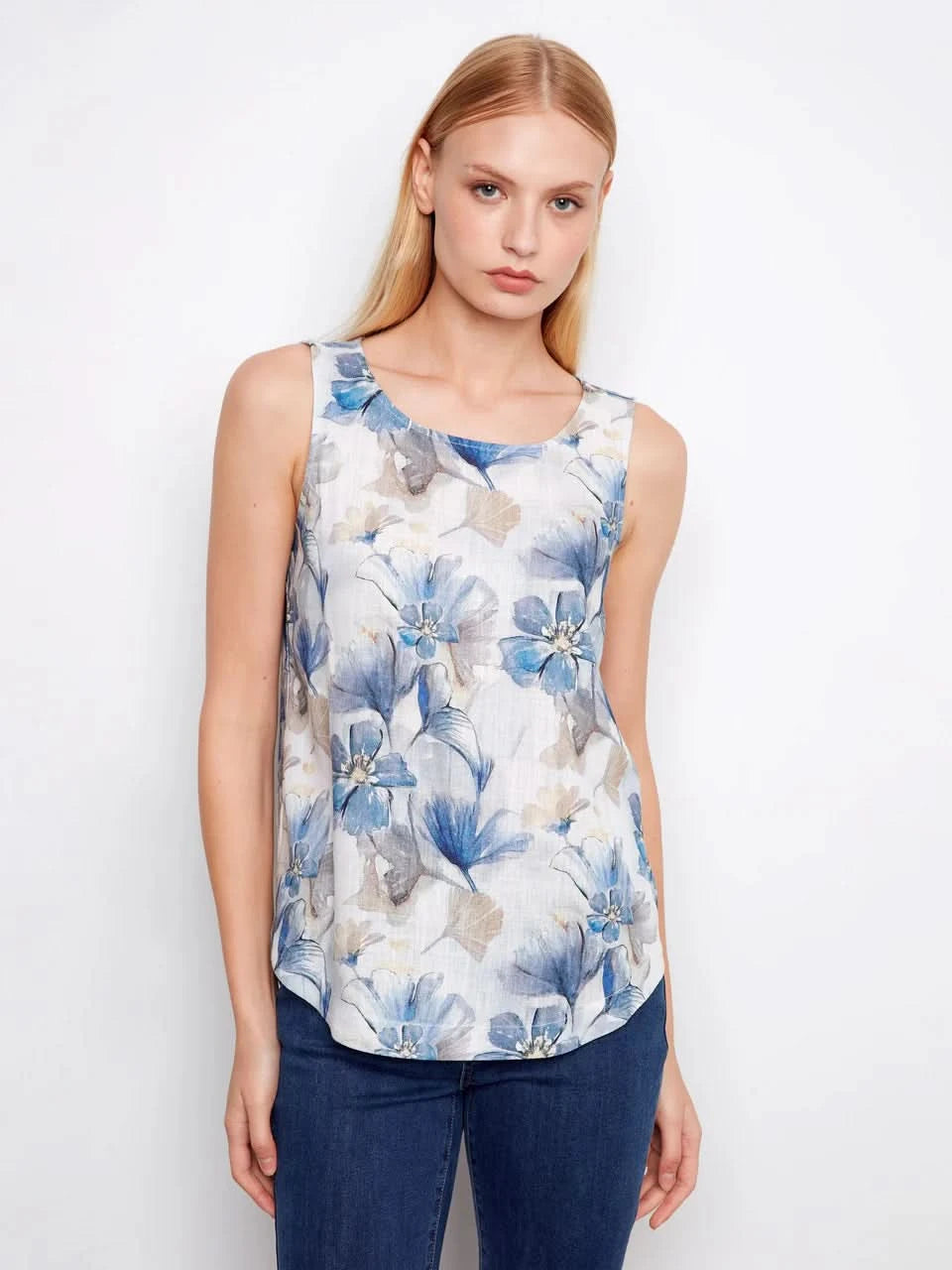 A woman models the Charlie B Printed Sleeveless Linen Blend Blouse, showcasing its blue floral print in gray tones against a plain white background.