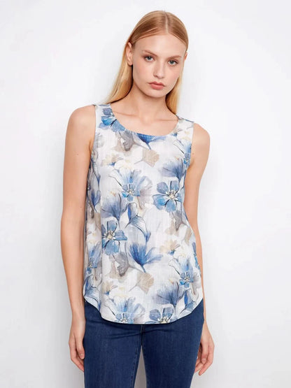 A woman models the Charlie B Printed Sleeveless Linen Blend Blouse, showcasing its blue floral print in gray tones against a plain white background.