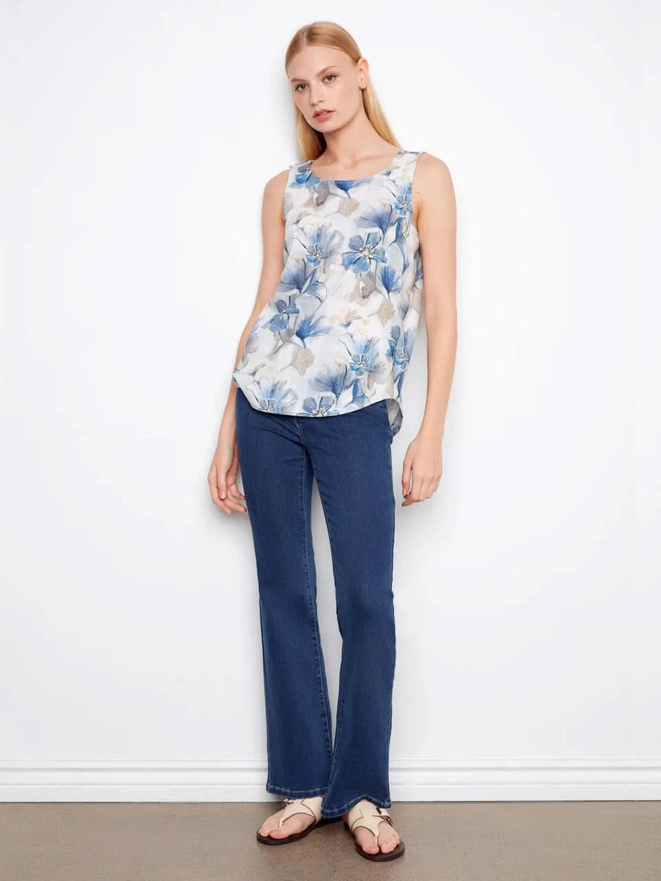 A woman models the Charlie B Printed Sleeveless Linen Blend Blouse, showcasing its blue floral print in gray tones against a plain white background.