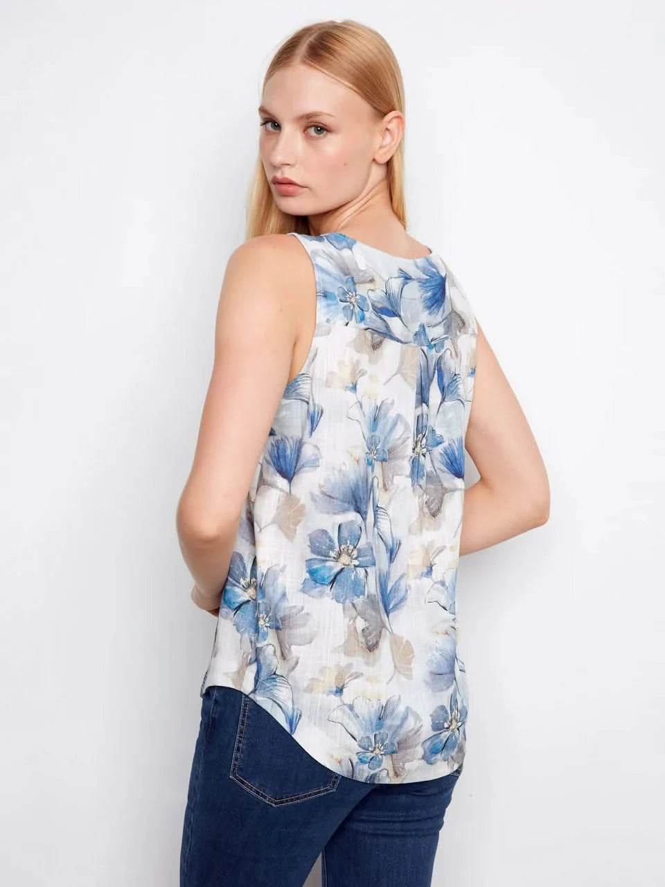 A woman models the Charlie B Printed Sleeveless Linen Blend Blouse, showcasing its blue floral print in gray tones against a plain white background.