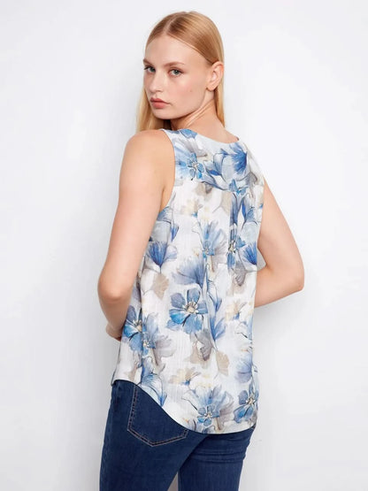 A woman models the Charlie B Printed Sleeveless Linen Blend Blouse, showcasing its blue floral print in gray tones against a plain white background.