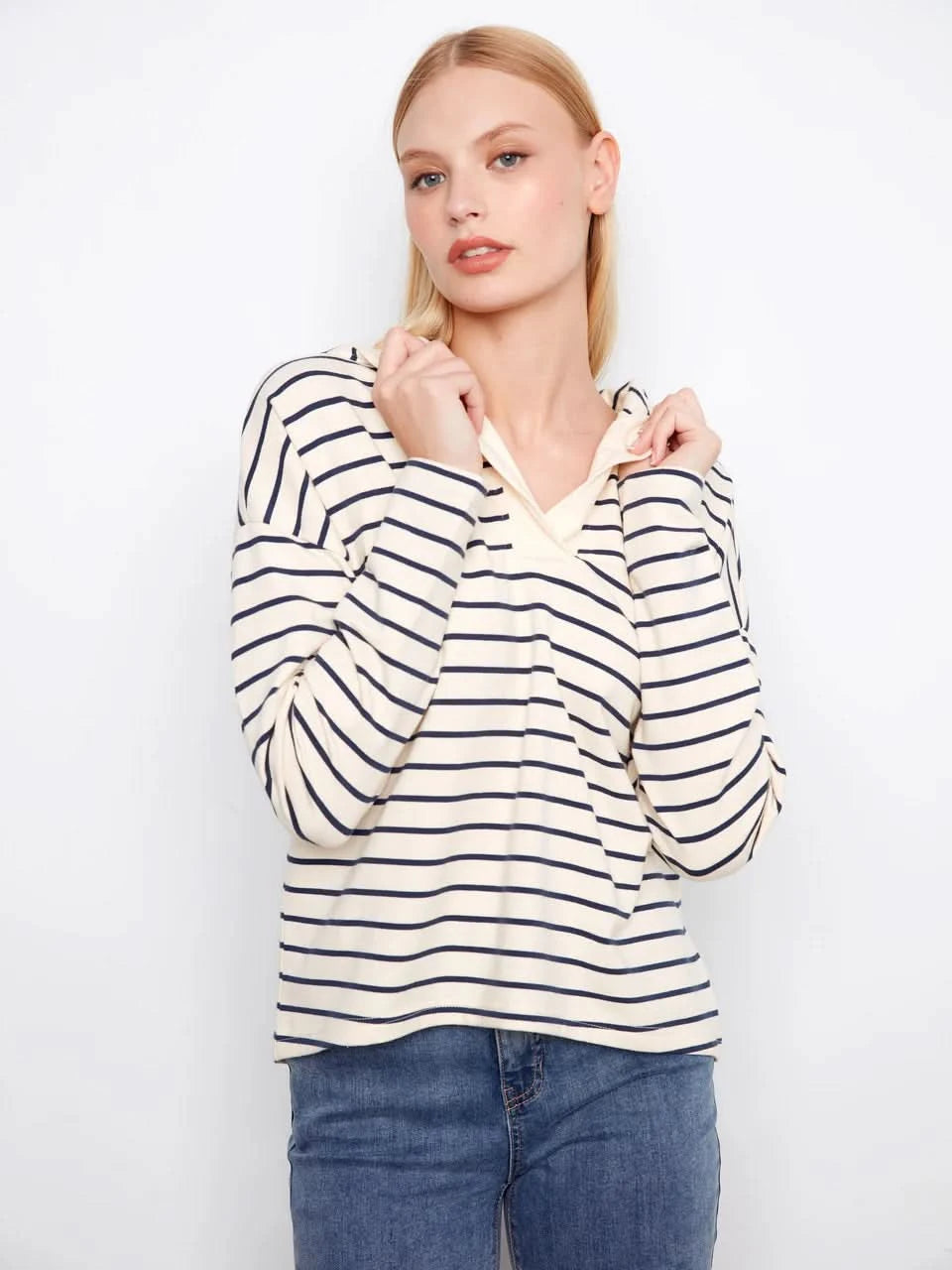 A person wears the Charlie B V-Neck Striped Hoodie, featuring cream and navy stripes and a relaxed cotton-spandex blend, standing against a plain white background.