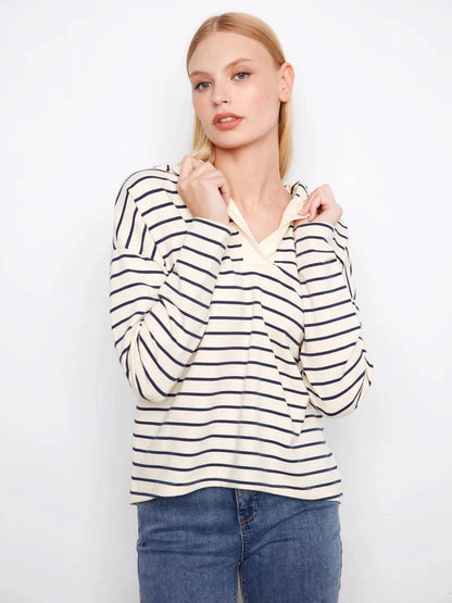 A person wears the Charlie B V-Neck Striped Hoodie, featuring cream and navy stripes and a relaxed cotton-spandex blend, standing against a plain white background.