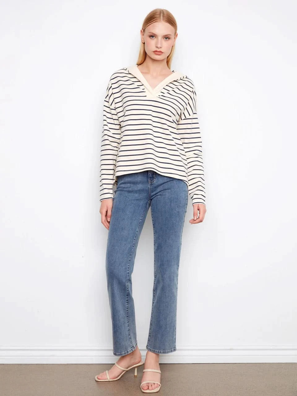 A person wears the Charlie B V-Neck Striped Hoodie, featuring cream and navy stripes and a relaxed cotton-spandex blend, standing against a plain white background.