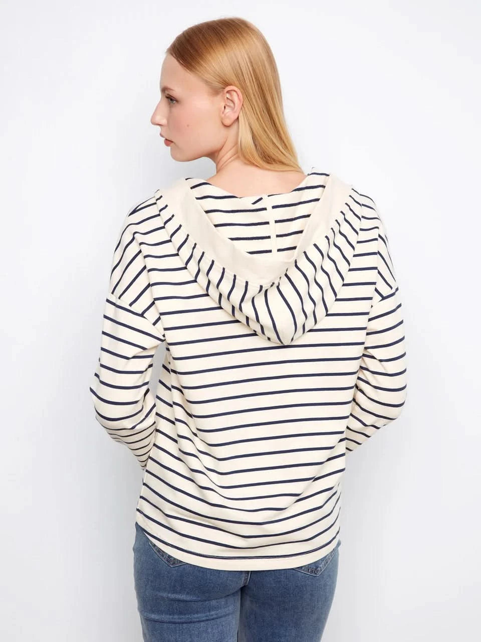 A person wears the Charlie B V-Neck Striped Hoodie, featuring cream and navy stripes and a relaxed cotton-spandex blend, standing against a plain white background.