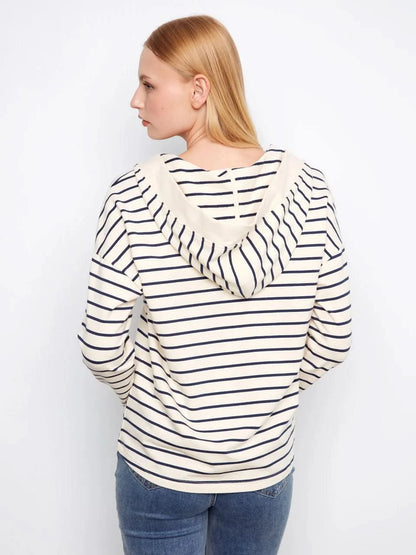 A person wears the Charlie B V-Neck Striped Hoodie, featuring cream and navy stripes and a relaxed cotton-spandex blend, standing against a plain white background.