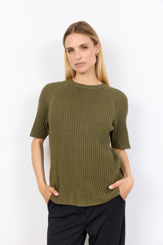 A person wearing the Soya Concepts Dark Olive Long Sleeved Knit in a relaxed fit with black pants stands against a plain white background, hands in pockets.