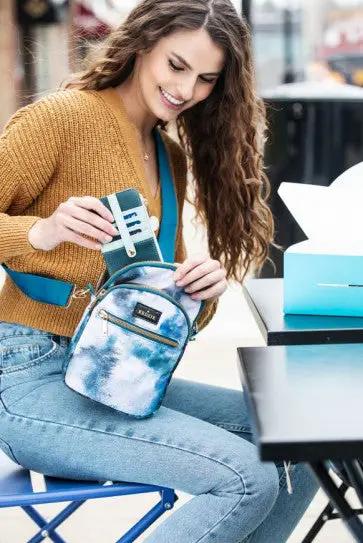 A woman sitting on a bench with a blue Kedzie Slim Zippered Wallet that has card slots.