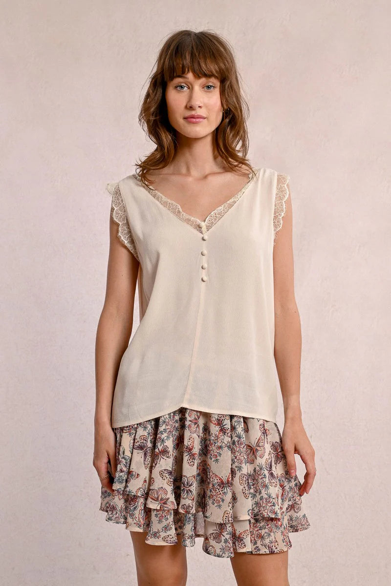 A woman embodies feminine elegance in Molly Bracken's Lace Camisole, a cream sleeveless top with delicate lace trim around the v-neckline and a row of small buttons down the front.