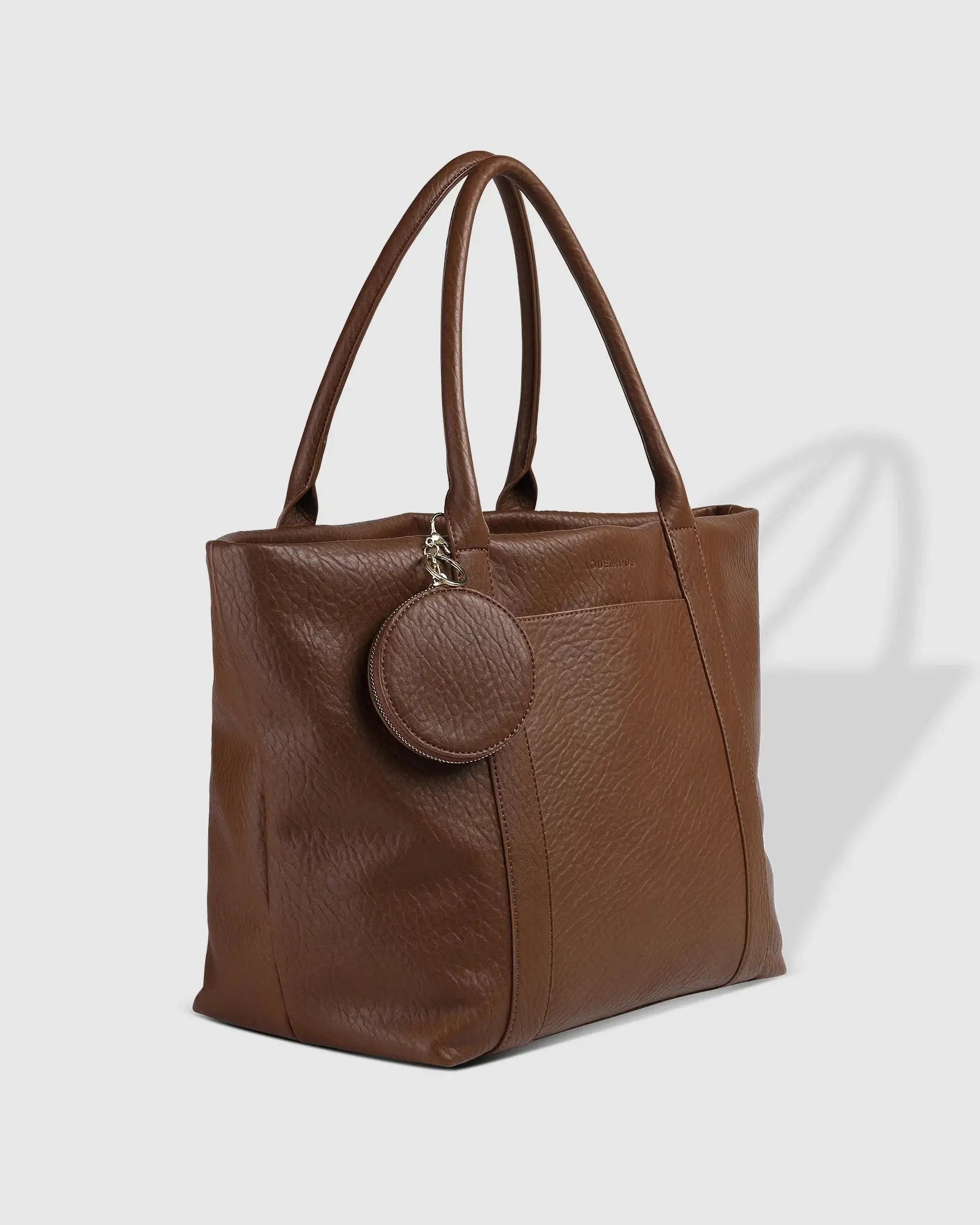 A person in white clothing stands on a porch holding The Savannah Tote Bag by Louenhide, crafted from vegan leather, resting it atop a black rolling suitcase.
